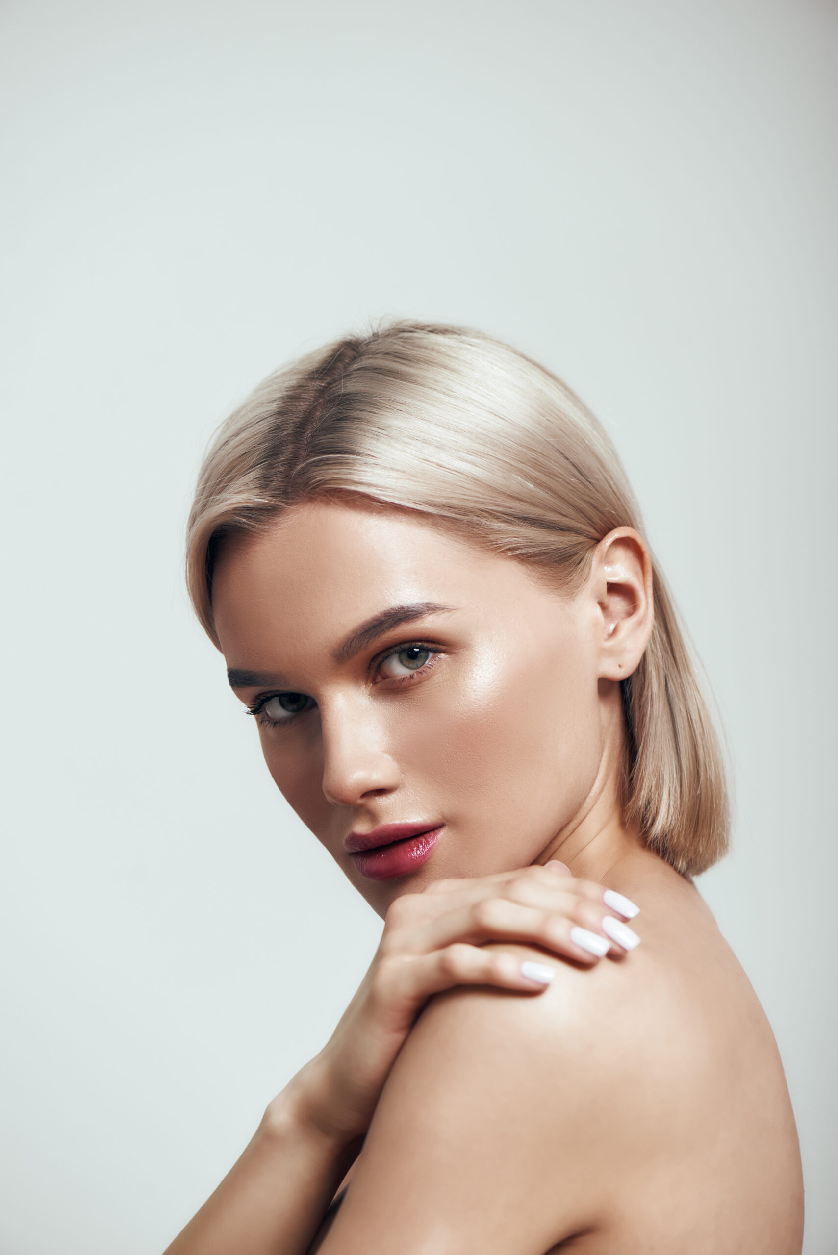 Perfection. Vertical photo of sexy young woman with blond hair and perfect shiny skin looking at camera while standing against grey background. Women beauty. Skin care. Studio shot